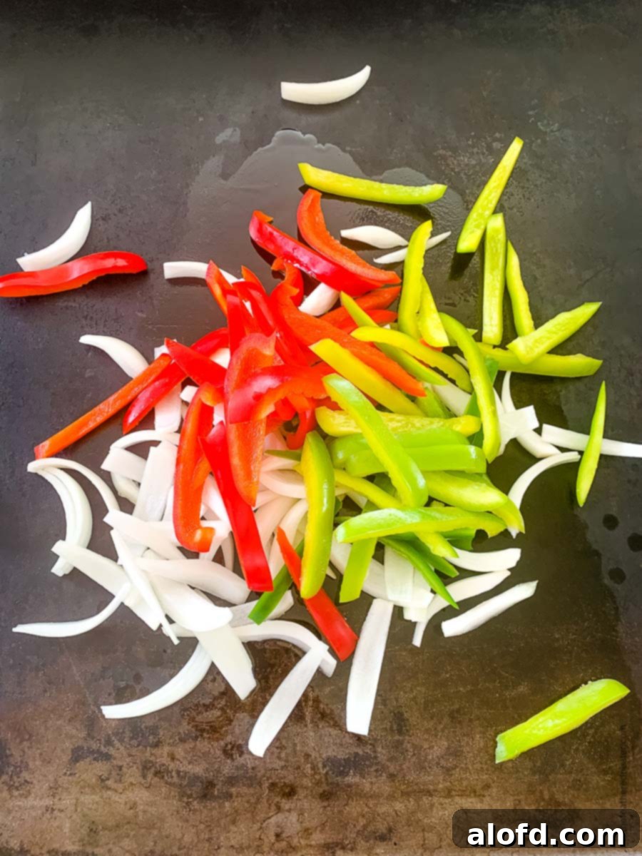 Vibrant bell peppers, jalapeno, and onions sizzling and caramelizing on a hot griddle, creating a delicious aroma.