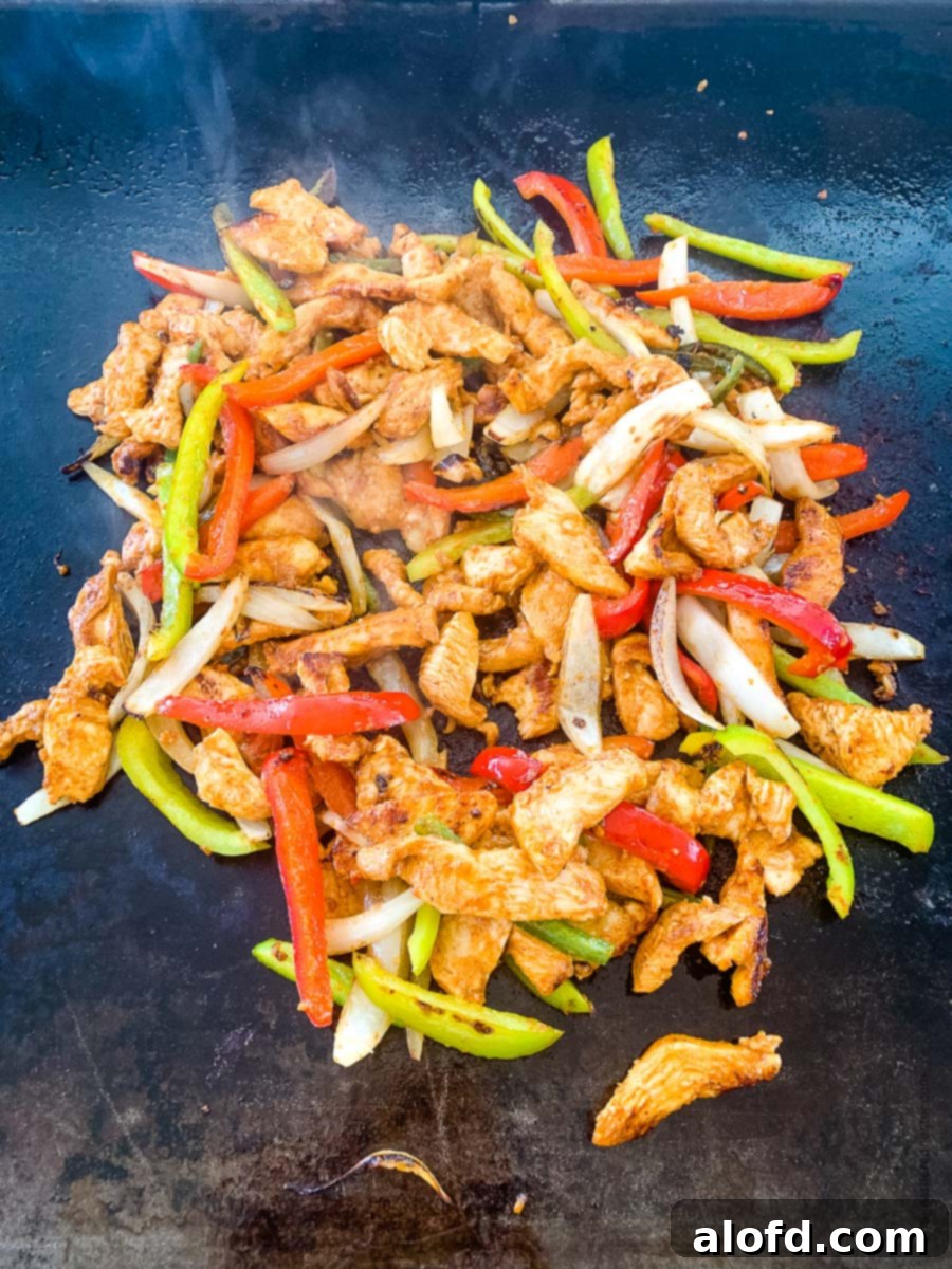 A delectable mixture of marinated chicken fajitas and colorful vegetables cooking together on a griddle, creating a harmonious blend of flavors.