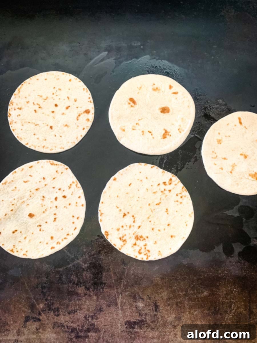 Soft flour tortillas being warmed on top of a Blackstone griddle, perfect for serving with hot fajitas.