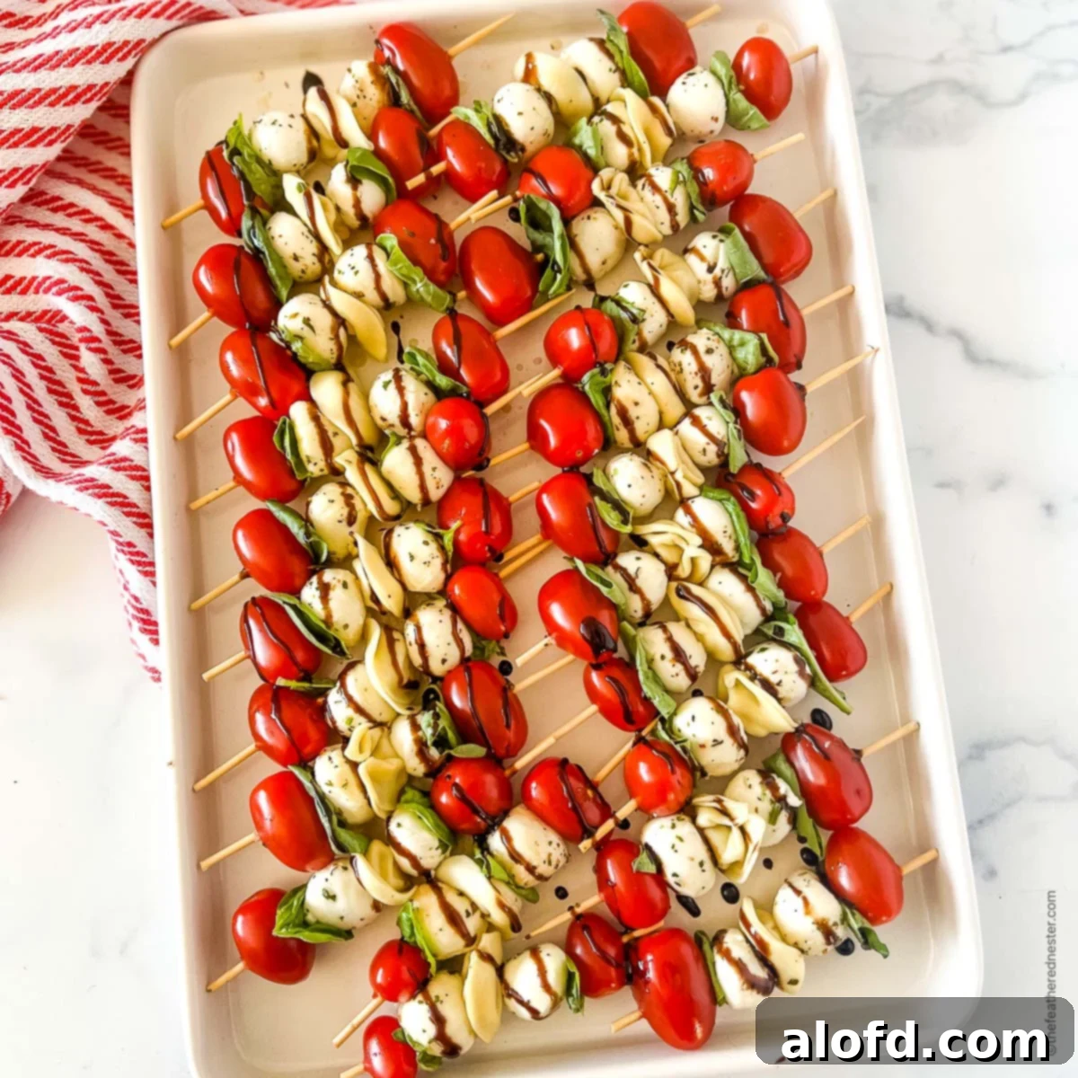 Caprese Tortellini Poppers 3 A white tray of kabob party appetizers with balsamic glaze on top of a red and white napkin.