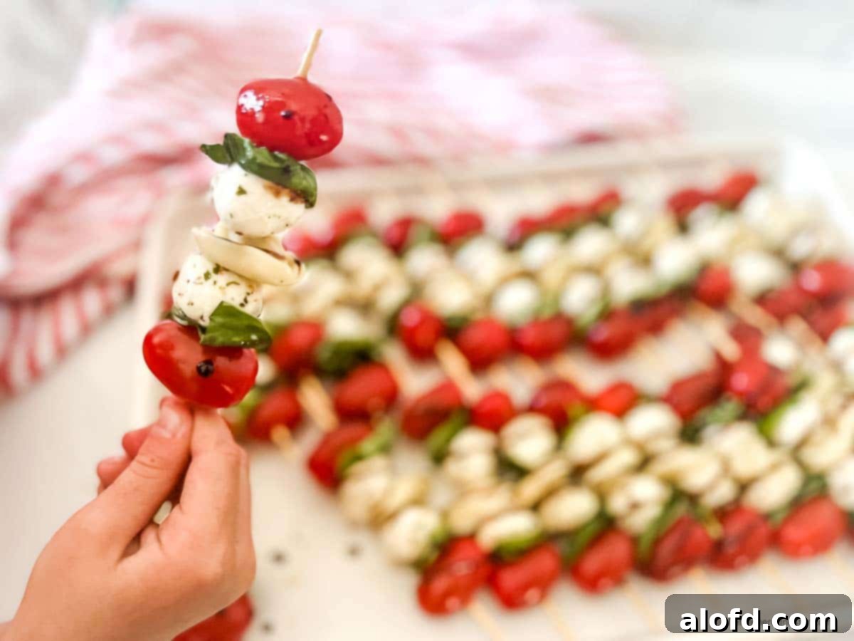 Caprese Tortellini Poppers 5 A closeup of a caprese tortellini appetizer with a tray of caprese skewers with balsamic drizzle and a red and white napkin in the background