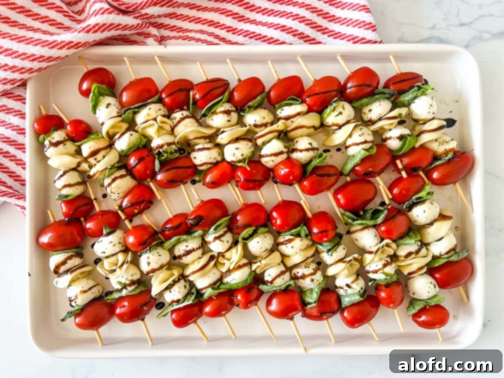 Caprese Tortellini Poppers 9 A white tray of tortellini skewers with balsamic glaze on top of a red and white napkin