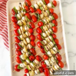 Caprese Tortellini Poppers 10 A white tray of kabob party appetizers with balsamic glaze on top of a red and white napkin.