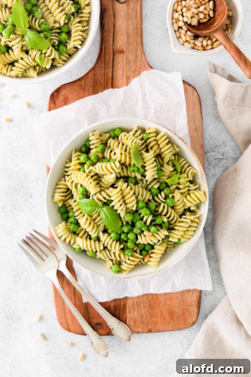 Spring Pea Pasta 2 A light summer meal of pasta with peas on a wooden serving board, accompanied by silverware and a small dish of pine nuts.