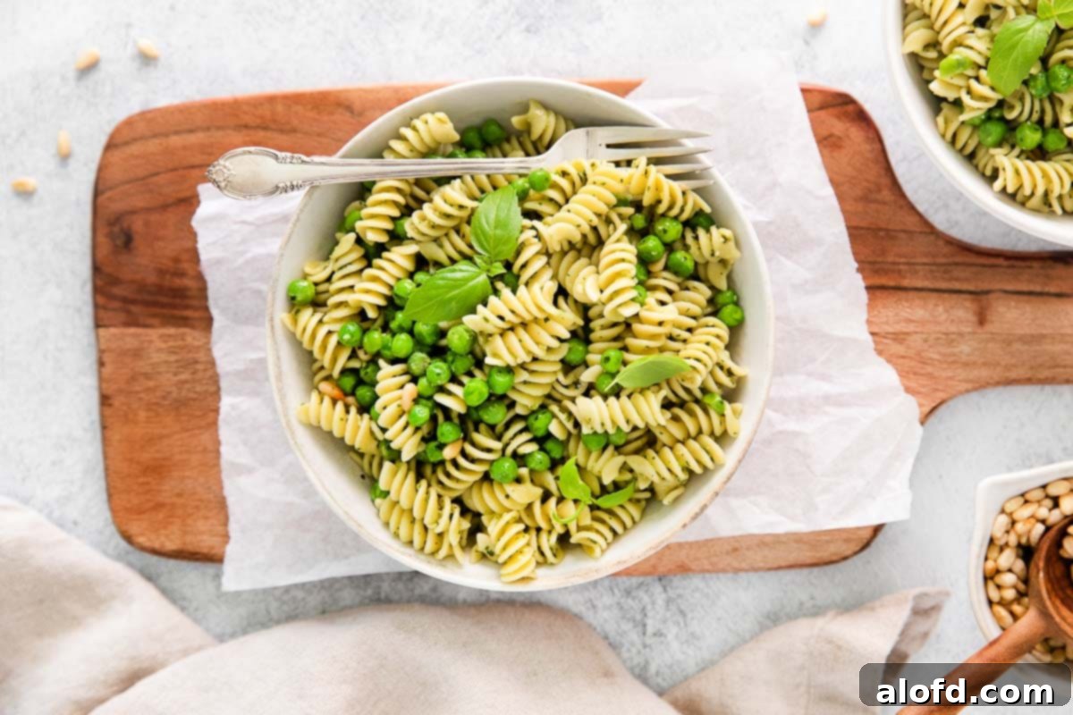 Spring Pea Pasta 12 A beautifully arranged bowl of pesto pasta with vibrant green vegetables, elegantly placed on a wooden serving board.