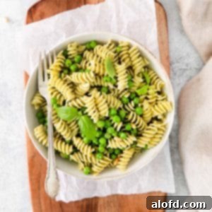 Spring Pea Pasta 13 A fork in a serving bowl of pesto pasta with green vegetables, garnished with fresh basil leaves.