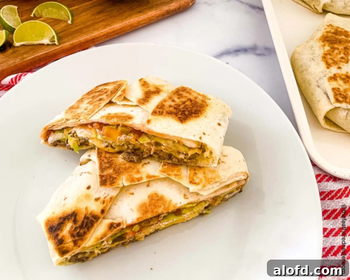 Blackstone's Ultimate Crunchwrap 9 A perfectly golden crunchwrap on a white plate, with a second crunchwrap on a white tray and a rustic wooden serving board in the background, adorned with lime wedges, salsa, and sour cream in bowls.