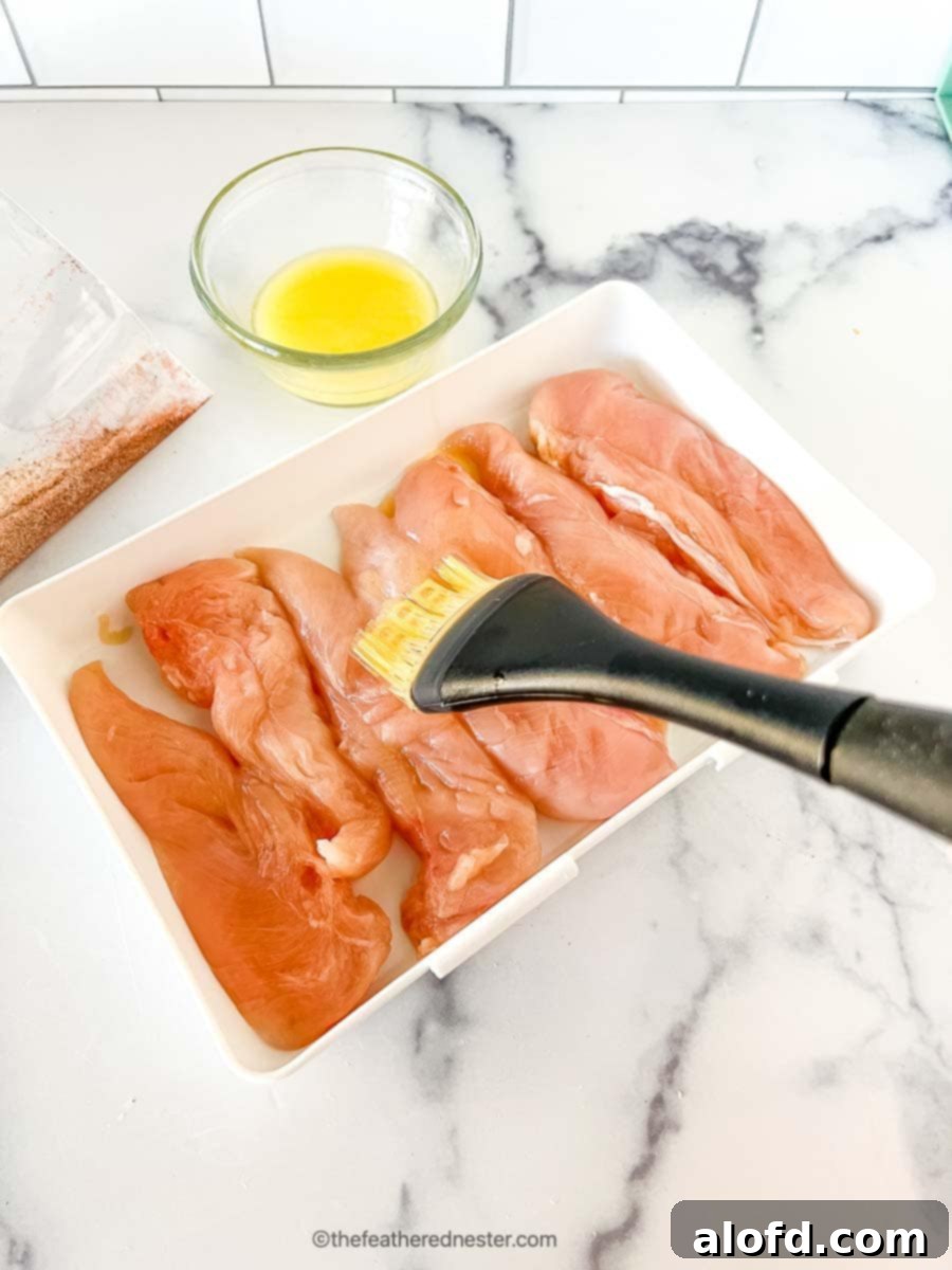 Basting melted butter to the chicken tenderloins on a casserole.