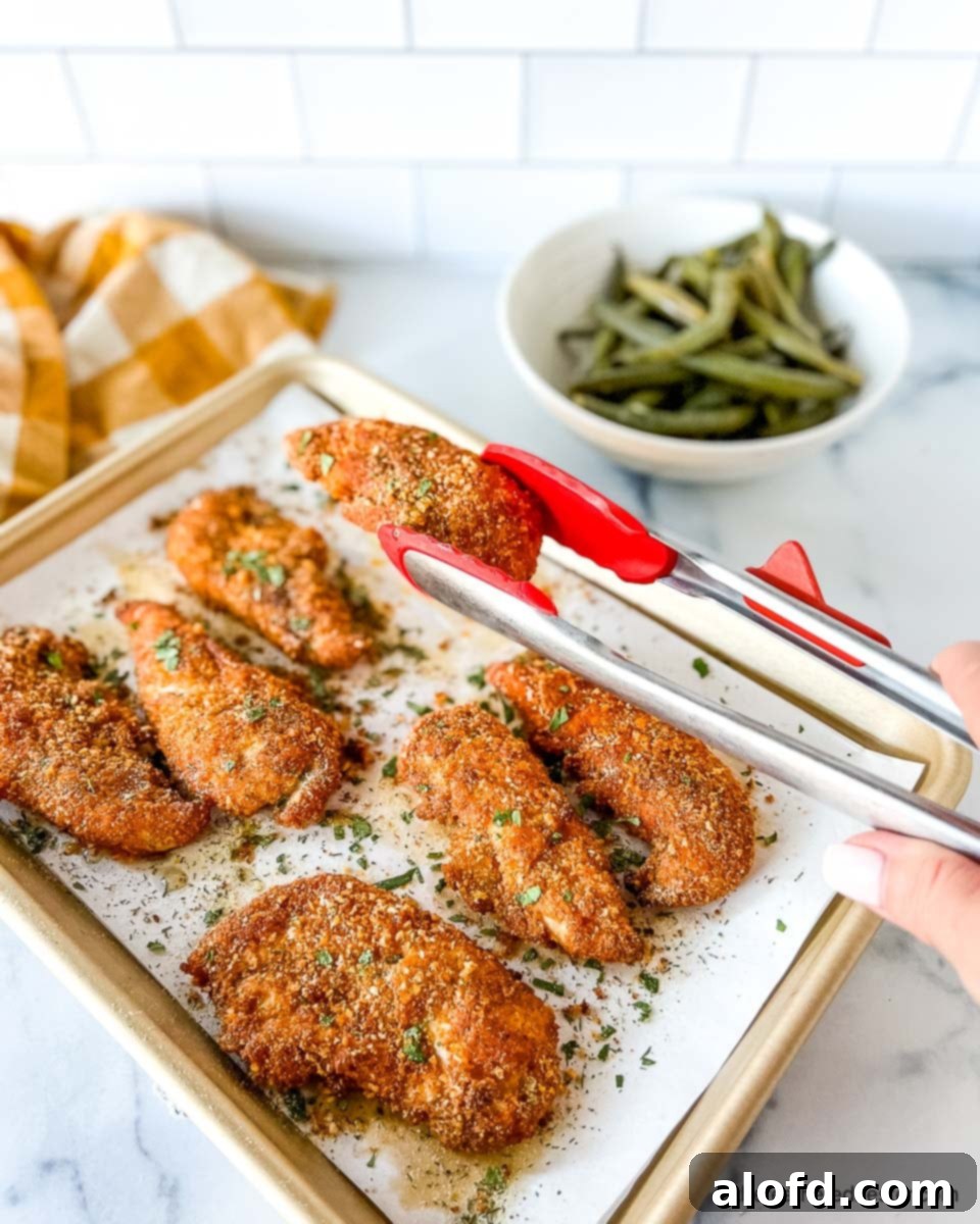 Cooked shake and bake chicken tenders on top of a parchment paper lined baking sheet.