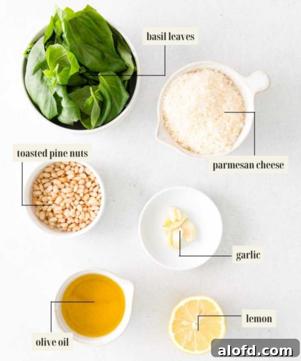 Emerald Herb Pesto 3 A collection of fresh, high-quality ingredients laid out for basil pesto sauce: fresh basil leaves, toasted pine nuts, whole garlic cloves, a lemon, a block of Parmesan cheese, and a bottle of extra virgin olive oil.