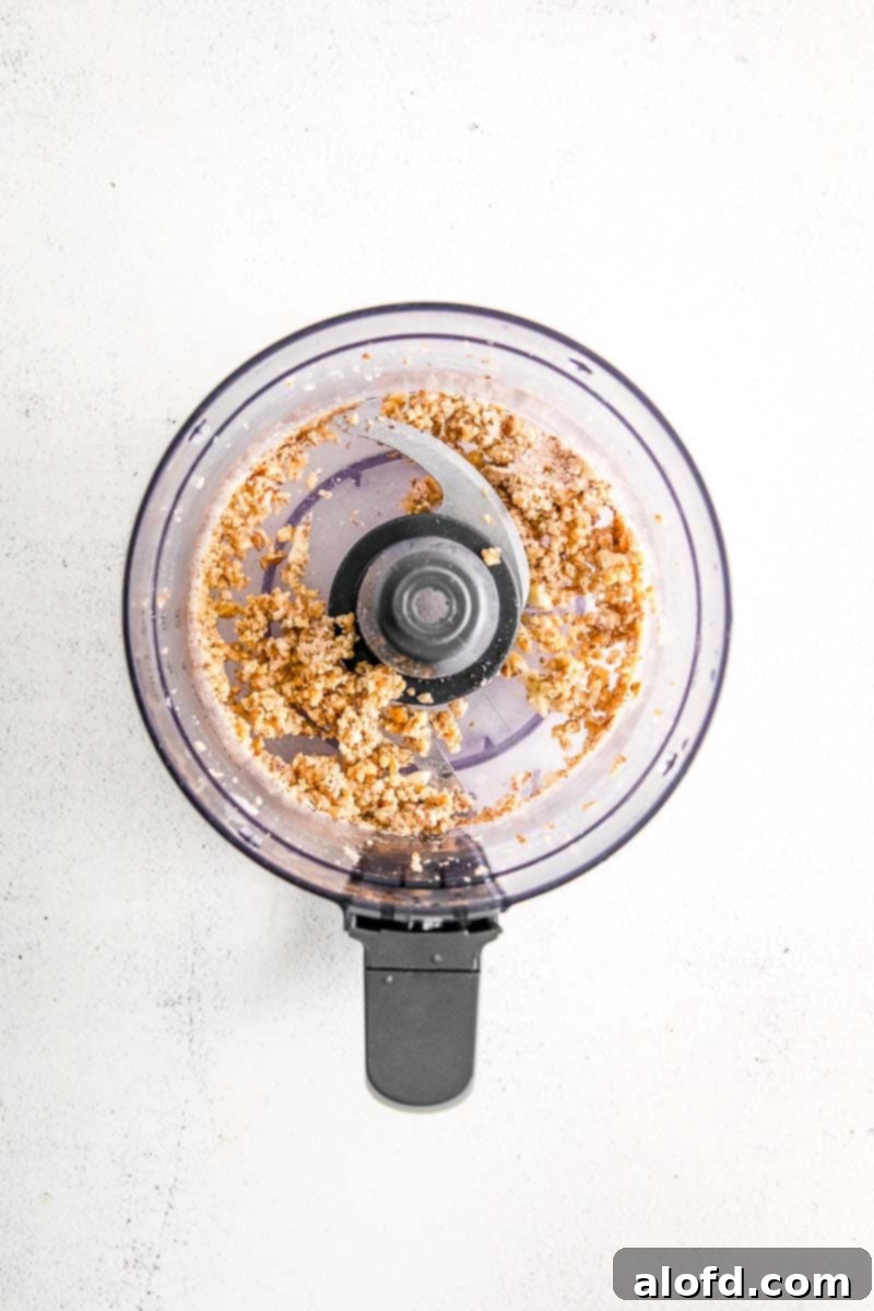 Emerald Herb Pesto 4 Close-up image of pine nuts, garlic, and lemon juice being blended together in a food processor, creating a coarse, aromatic mixture.