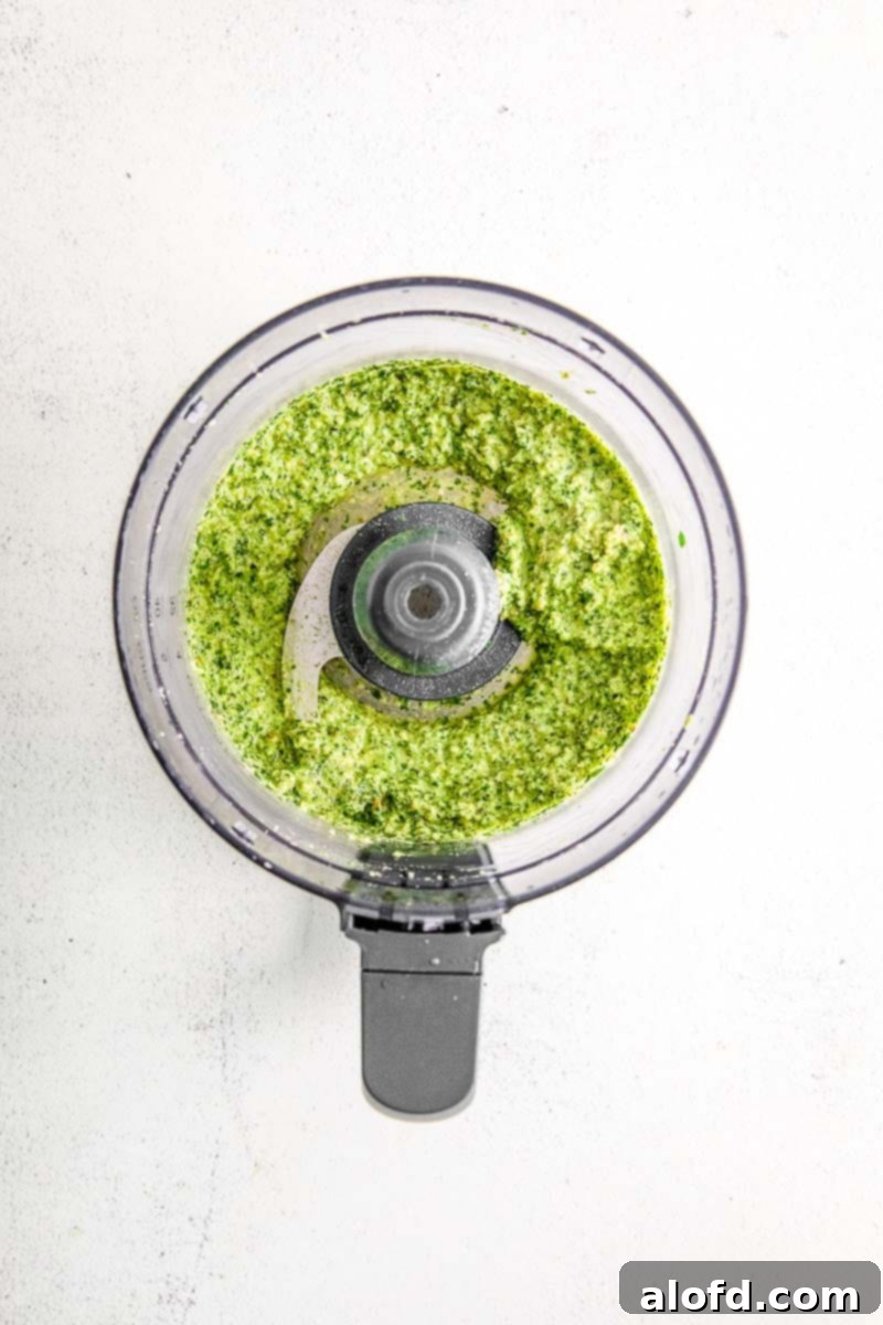 Emerald Herb Pesto 6 The food processor blending all the pesto ingredients together with olive oil, creating a smooth, vibrant green basil pesto sauce.