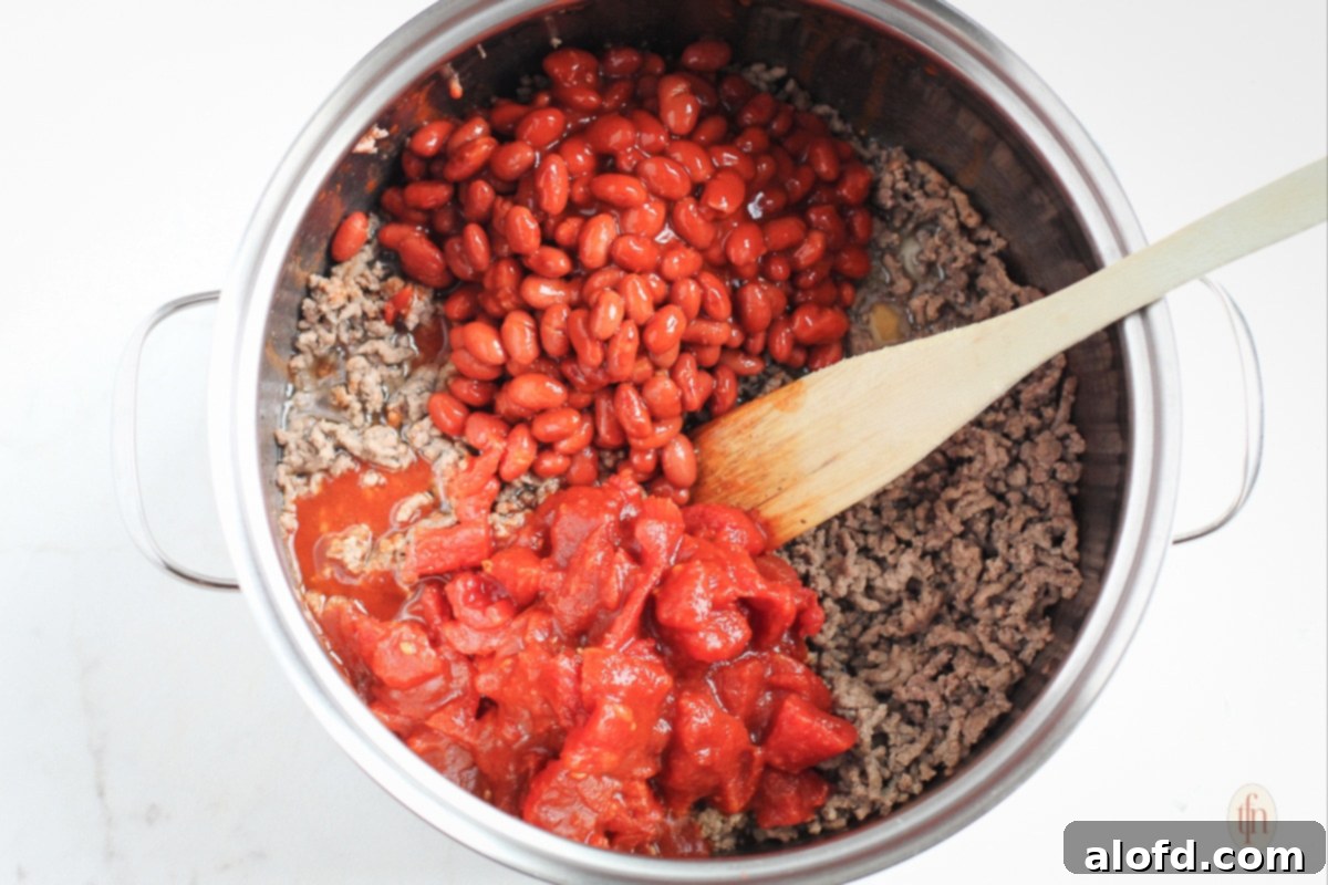 Hearty Skillet Chili 6 Diced tomatoes, kidney beans, and browned ground beef in a large pot with a wooden spoon.