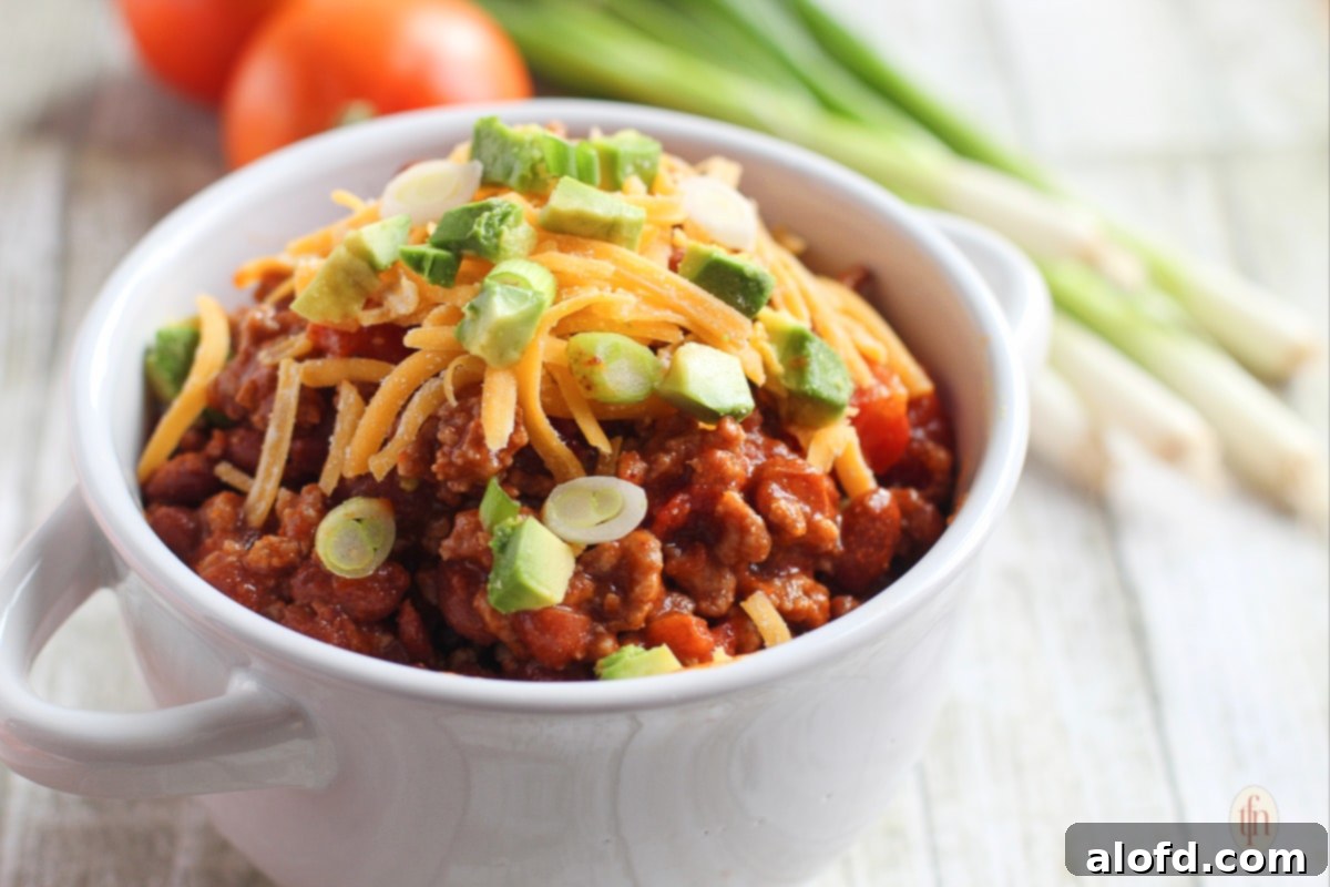 Hearty Skillet Chili 8 Serving of Dutch oven chili in a white bowl, garnished with grated cheddar cheese and chopped green onions.