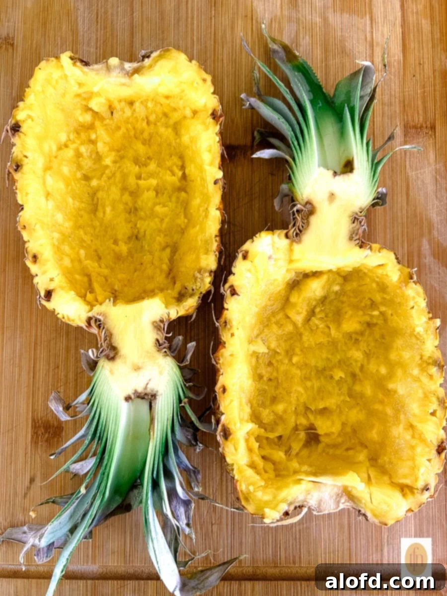 An empty, hollowed pineapple bowl resting on a wooden cutting board, ready for filling.