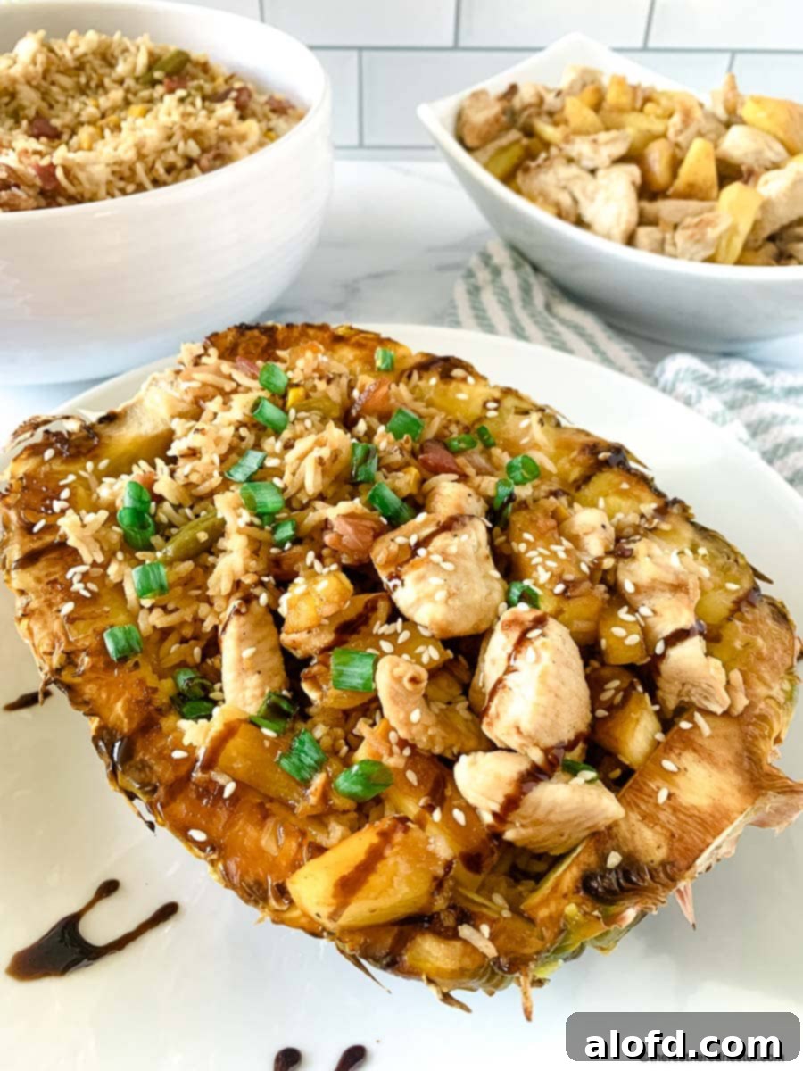 A beautifully arranged teriyaki chicken pineapple bowl with fried rice and a rich glaze, accompanied by extra pineapple chunks and chicken in the background.