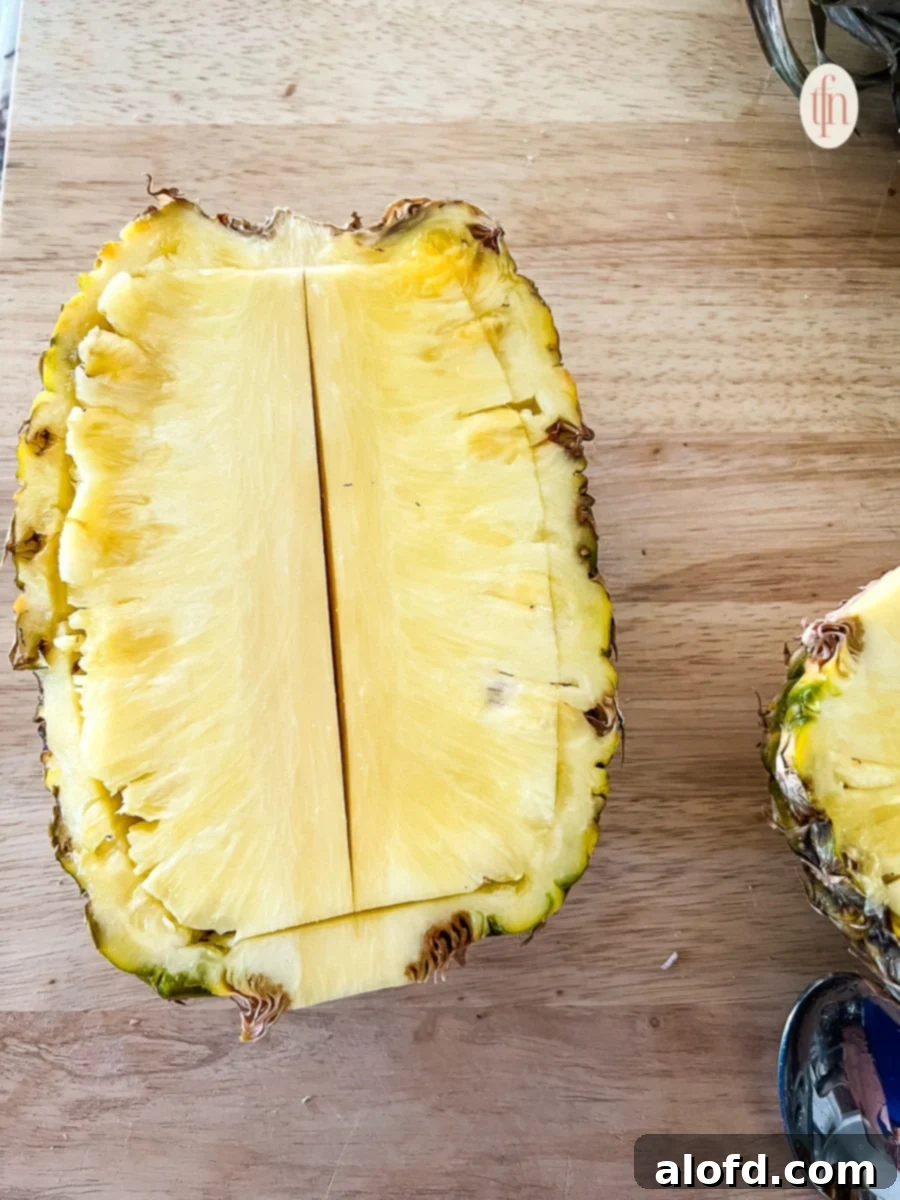One half of a pineapple showing knife cuts made to loosen the core and flesh from the shell.