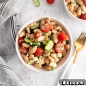 Vibrant Italian Bean Medley 11 A white bowl of Tuscan bean salad with silverware to the right and a striped napkin on the left.