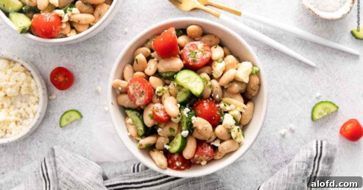 Vibrant Italian Bean Medley 10 A beautifully composed flat lay of a white bowl of Tuscan bean salad, with silverware, a striped napkin, and another bowl in the background.