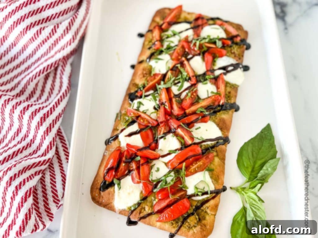 Classic Margherita Flatbread 9 A white serving tray with a baked tomato basil flatbread, garnished with a sprig of fresh basil, placed next to a red and white napkin.