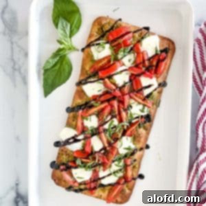 Classic Margherita Flatbread 10 A white serving tray with a baked Caprese flatbread pizza and a sprig of fresh basil next to a red and white napkin.