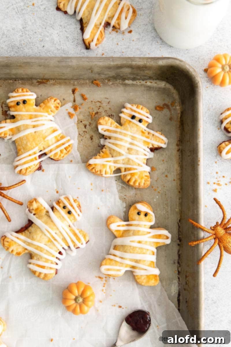 hand pies with berry filling on top of a parchment paper and baking sheet with spoon of berry jam, spider toy, pumpkin toy in the background