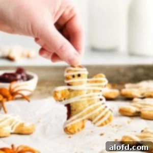 a hand holding a mummy hand pie placed on a parchment paper and baking sheet with spider toy, pumpkin toy and a bowl of berry filling at the background.