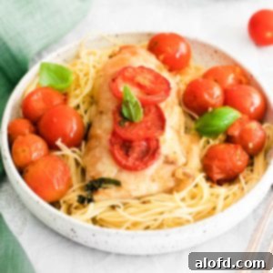 One Pan Caprese Chicken 12 a white bowl of pasta with a chicken breast and roasted cherry tomatoes and basil on top with a white bowl of cherry tomatoes in the background.