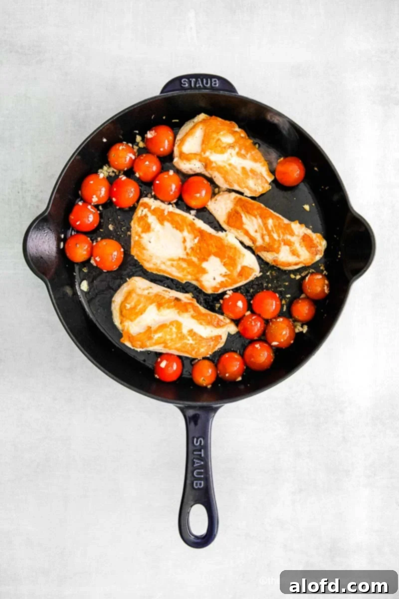 One Pan Caprese Chicken 7 A Staub cast iron skillet with sautéed chicken breasts and cherry tomatoes.