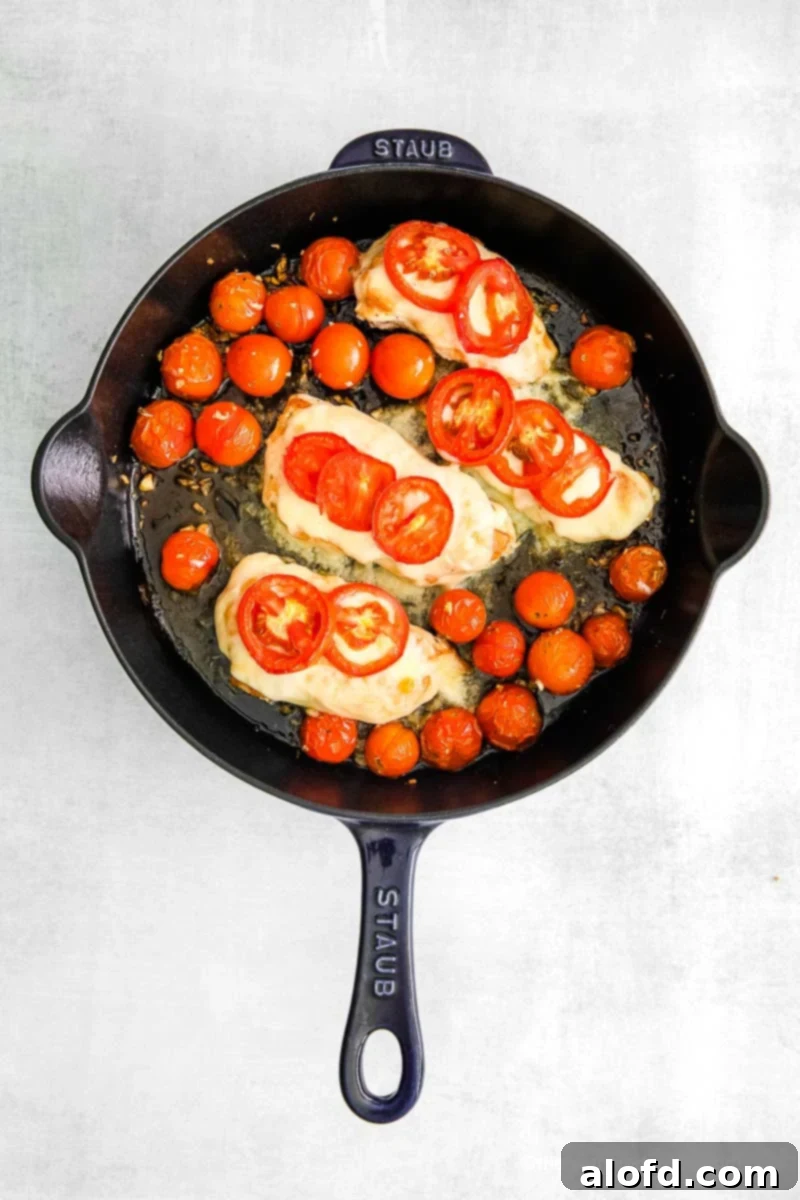 One Pan Caprese Chicken 8 a Staub cast iron skillet with sautéed chicken breasts topped with mozzarella cheese and cherry tomatoes