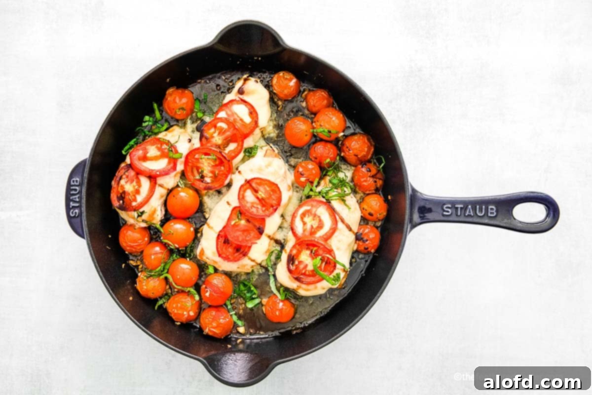 One Pan Caprese Chicken 9 A Staub cast iron skillet with sautéed chicken breasts and cherry tomatoes and basil.