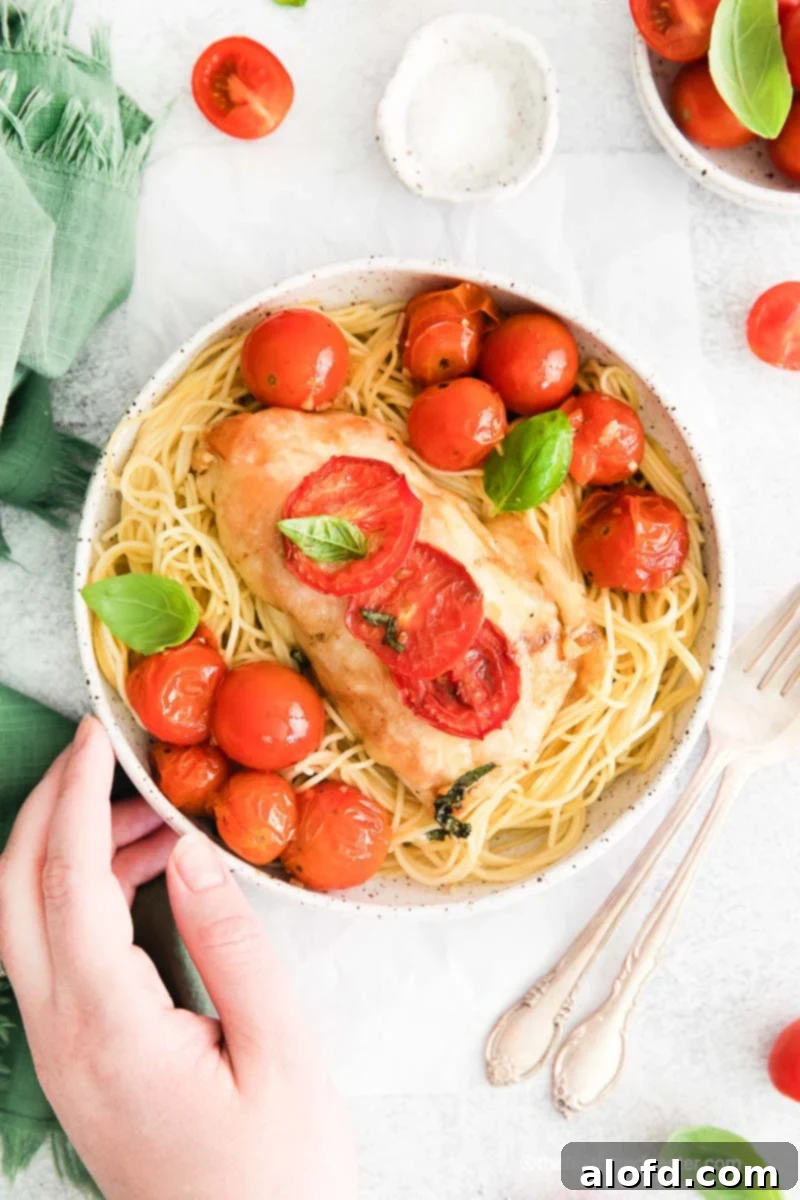 One Pan Caprese Chicken 10 A hand holding a white bowl of pasta with chicken breast.