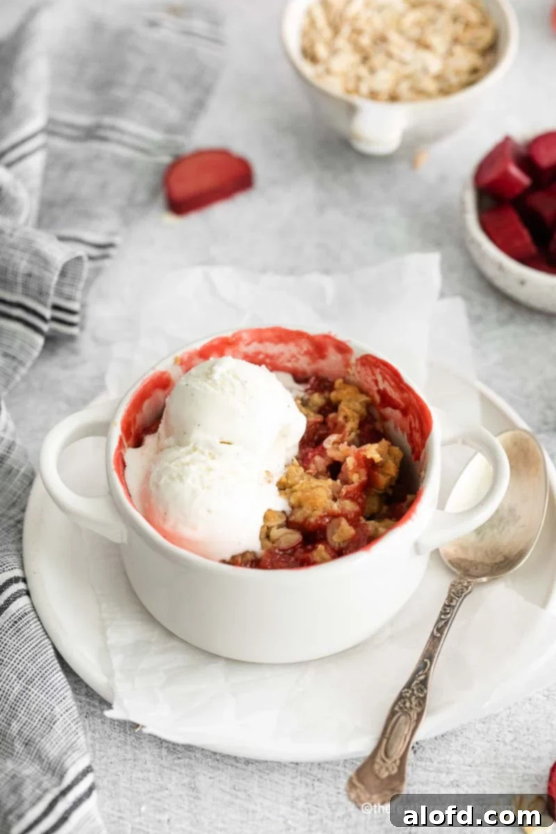 A ramekin of apple strawberry crisp topped with vanilla ice cream, served on a plate with parchment paper and a spoon.