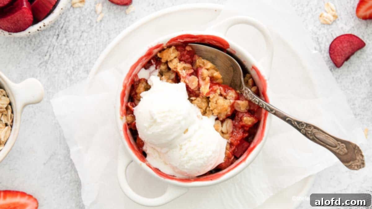 A white ramekin of apple strawberry crisp with vanilla ice cream on top, and a spoon ready to serve.