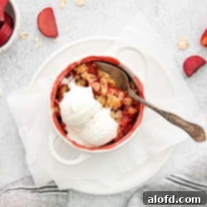 A white ramekin of apple strawberry crisp with vanilla ice cream on top, ready to be served.