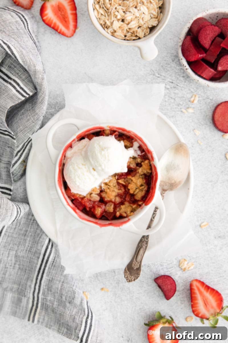Top-down view of an apple strawberry crisp with melting vanilla ice cream, surrounded by fresh strawberries and oats.