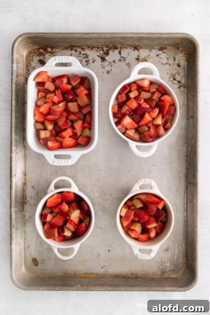 Ramekins and a casserole dish filled with chopped strawberries and apples on a baking tray.