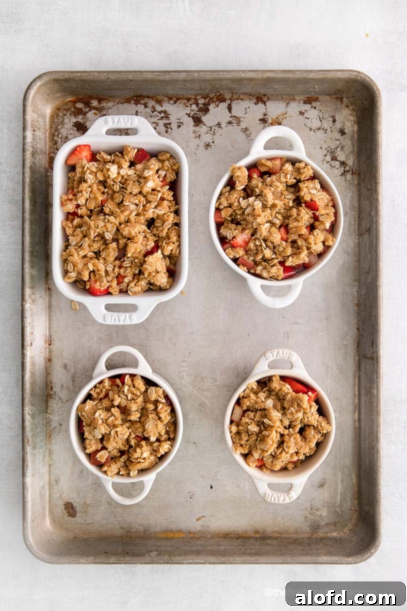 Prepared fruit layer and oat crumble topping in ramekins and a casserole dish on a baking tray.