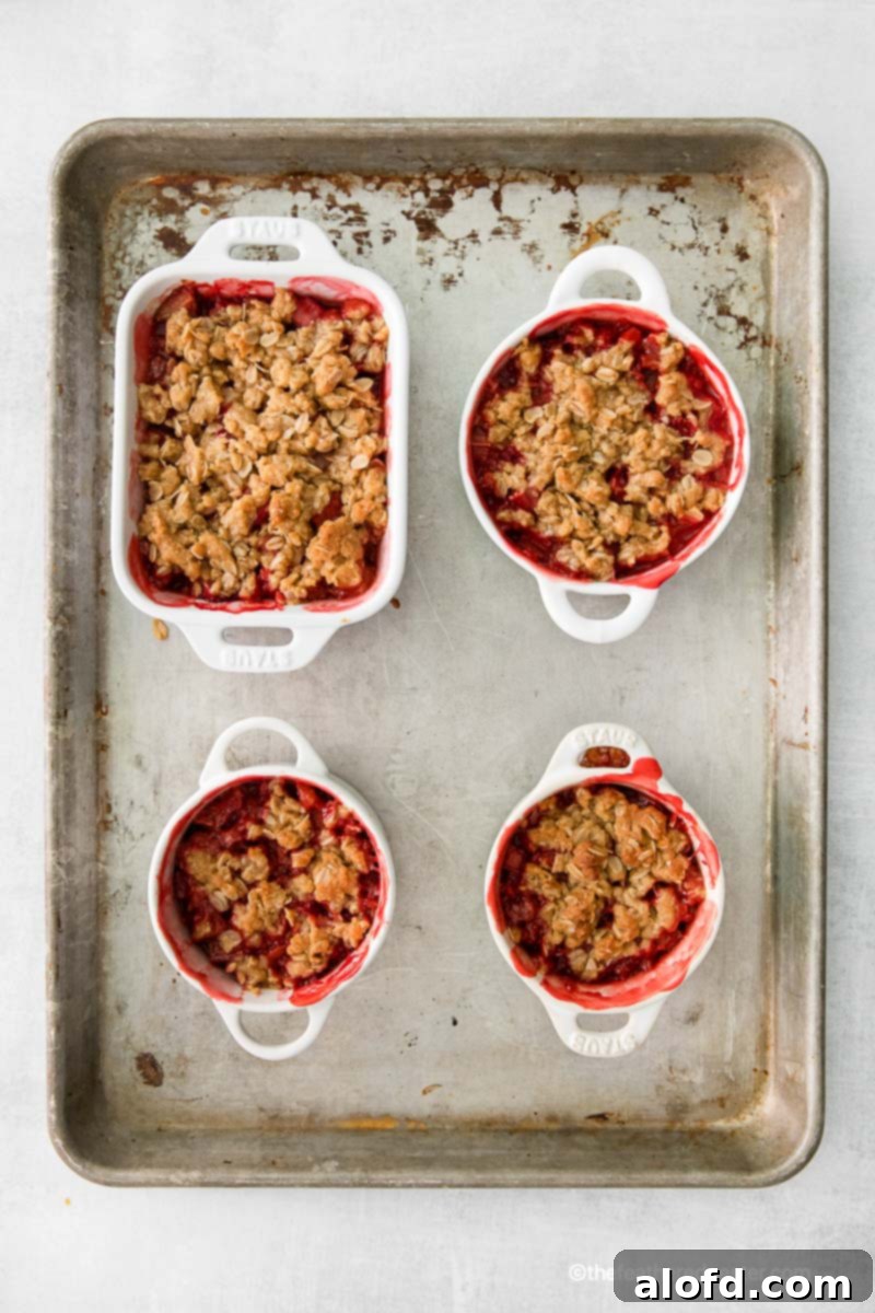 Baked apple strawberry crisps in ramekins and a casserole dish cooling on a baking tray.