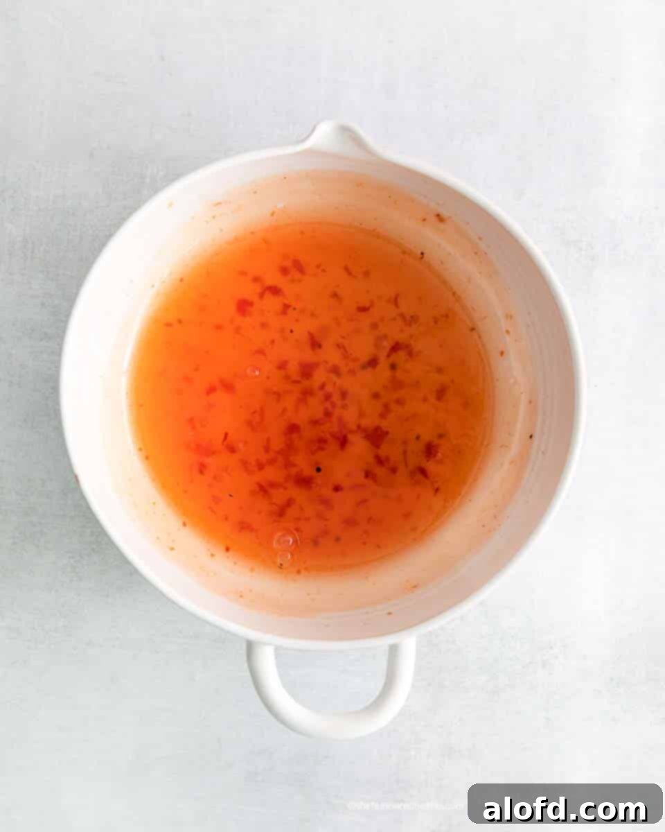 A mixing bowl filled with the vibrant orange sweet chili sauce, ready for the meatballs.