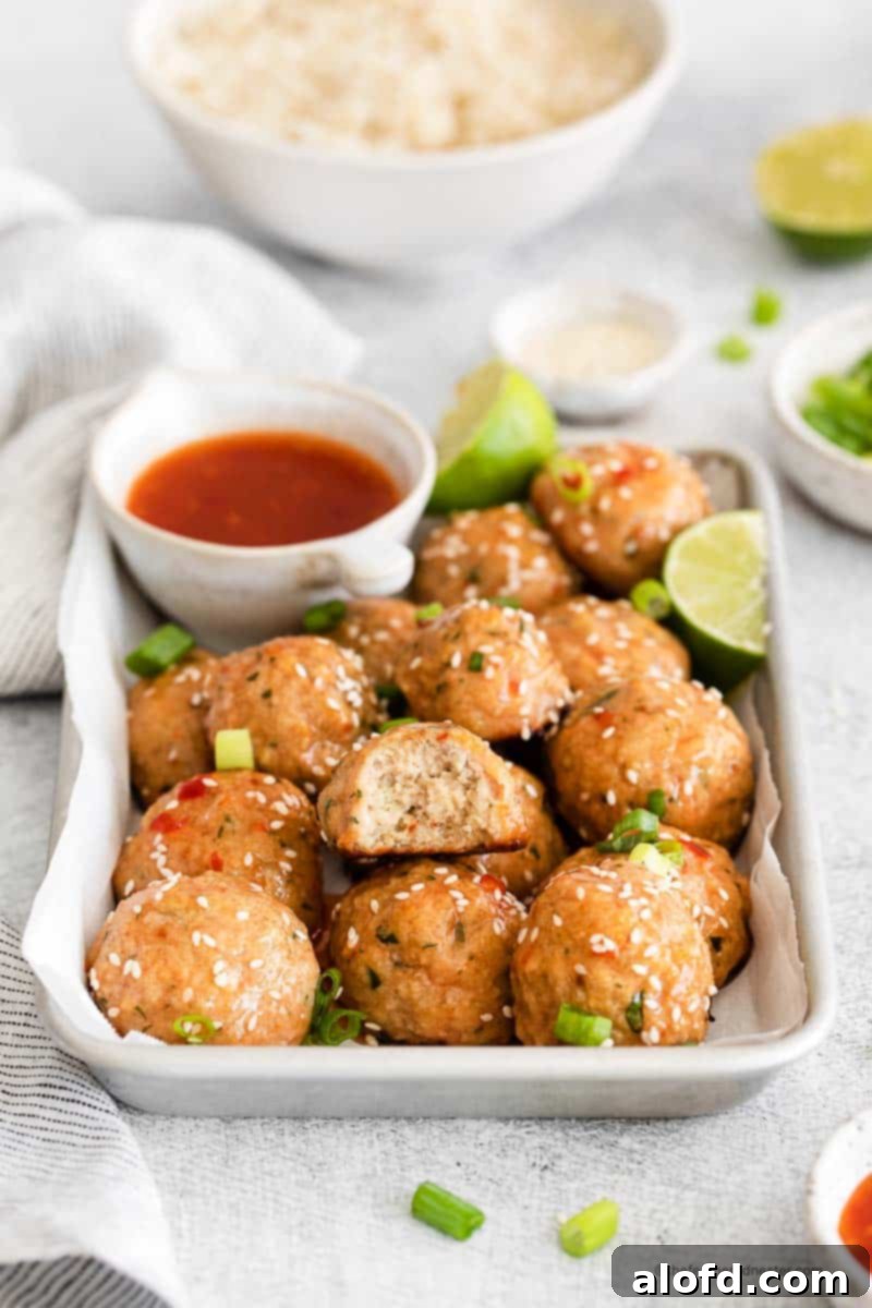 A baking sheet filled with golden brown sweet chili meatballs, garnished with fresh cilantro and vibrant sesame seeds. Beside it, a small bowl of chili sauce and a lime wedge hint at the zesty flavors.