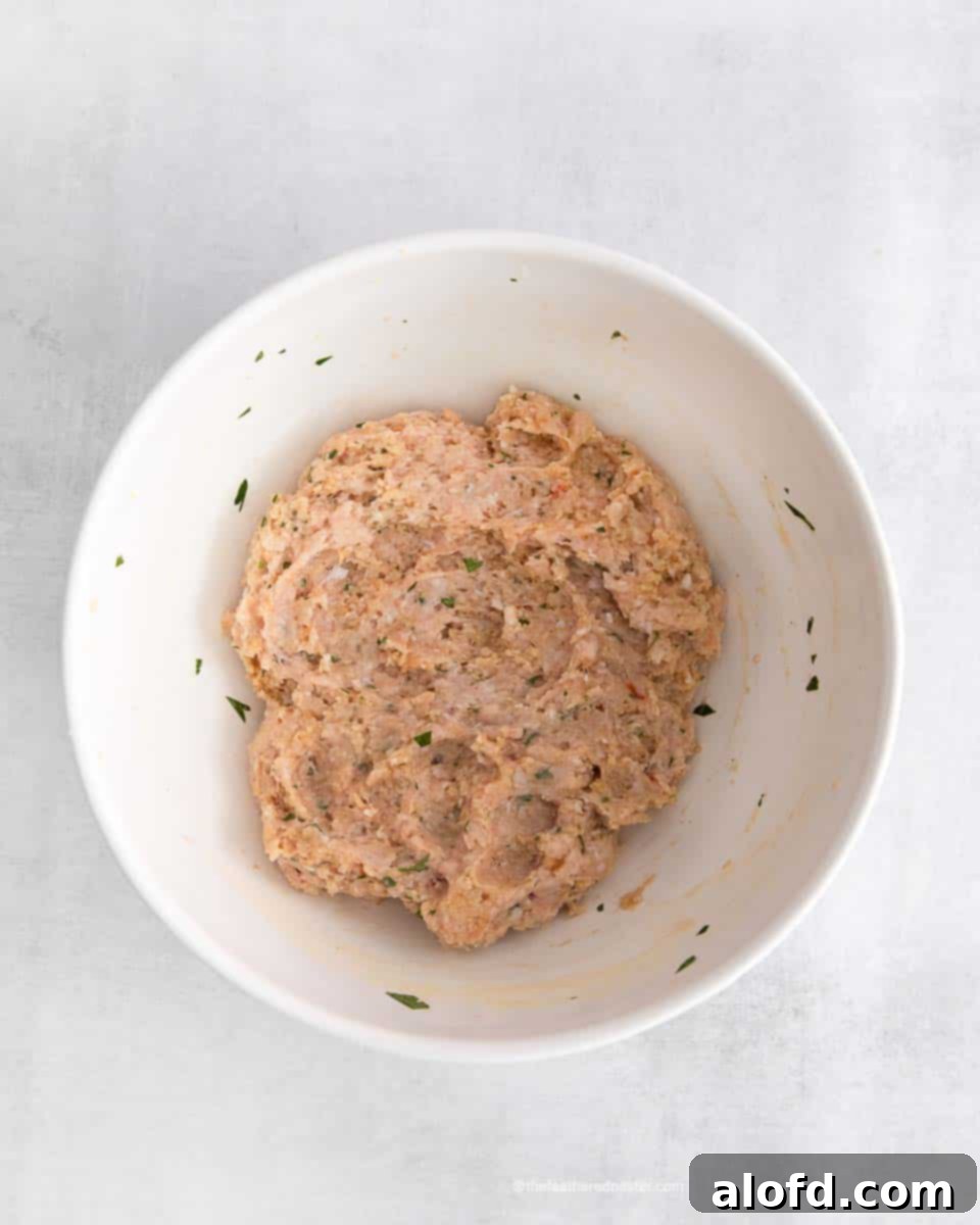 A white mixing bowl containing the perfectly combined raw chicken meatball mixture, showcasing the blend of ground chicken, herbs, and spices.