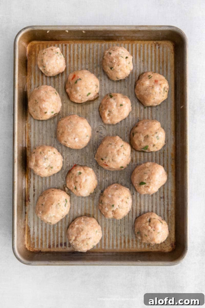 A baking sheet neatly arranged with uncooked, perfectly formed sweet chili meatballs, ready for baking.