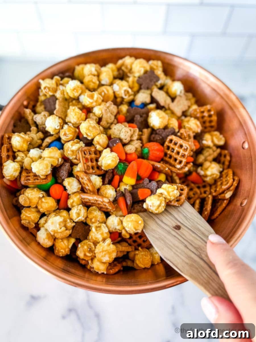 Monster Munch Mix 5 A close-up shot of someone gently stirring the Halloween snack mix ingredients in a large copper bowl with a wooden spoon, highlighting the vibrant colors and textures.