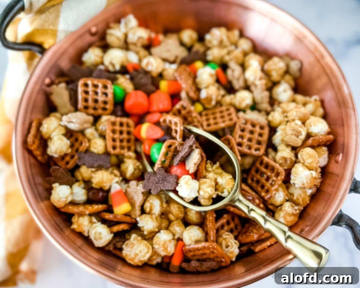 Monster Munch Mix 7 A large copper bowl of M&M Halloween snack mix, with a gold scoop invitingly placed inside, and a gold and white napkin providing a soft backdrop.
