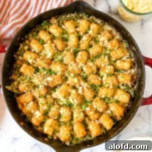 Savory Turkey Tater Bake 12 top view of turkey tater tot casserole in a cast iron skillet with red striped cloth and a jar of shredded cheese in the background.