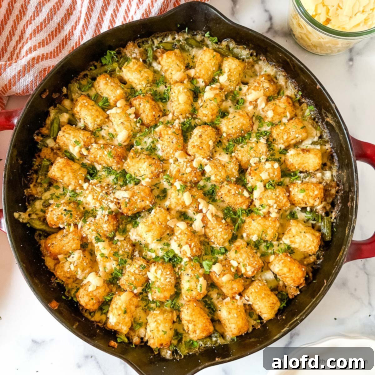 Savory Turkey Tater Bake 9 top view of turkey tater tot casserole in a cast iron skillet with red striped cloth and a jar of shredded cheese in the background.