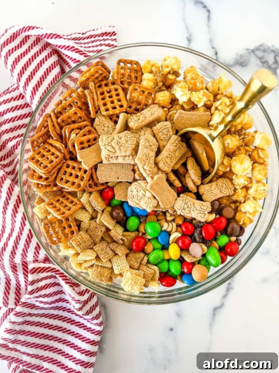 Irresistible M&M Chex Party Snack 5 A clear bowl filled with Chex party mix with M&M's and a golden scoop, showcasing the delicious blend of ingredients.