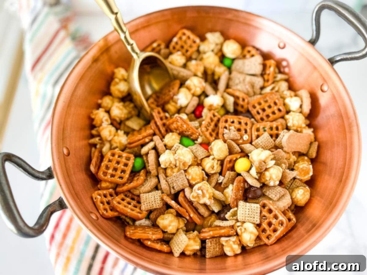 Irresistible M&M Chex Party Snack 6 A rustic wooden bowl filled with Chex Mix with M&M's, complete with a golden scoop, ready for guests to enjoy.