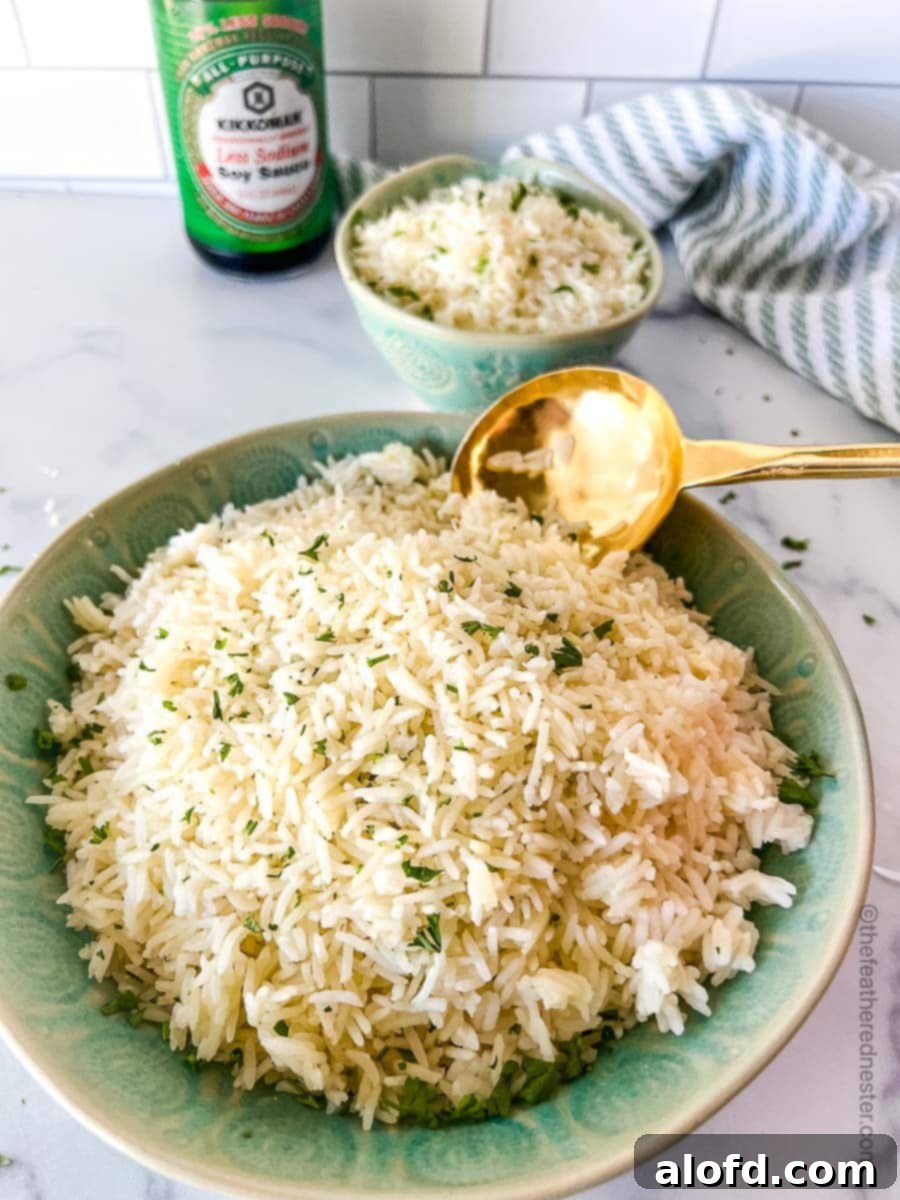 A large green bowl of perfectly cooked, fluffy Instant Pot Jasmine Rice with a golden serving spoon. In the background, a smaller bowl of rice, a striped cloth, and a bottle of soy sauce complete the inviting scene.